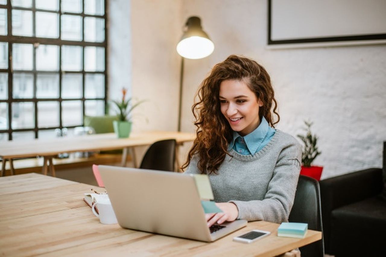 profissoes-freelancer - mulher em escritório com computador e sorrindo